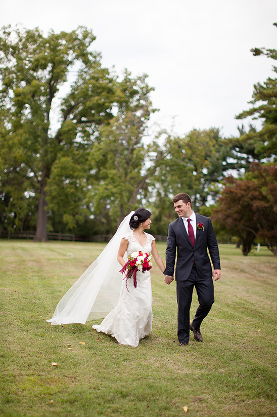 Newlyweds holding hands walk across a grassy field