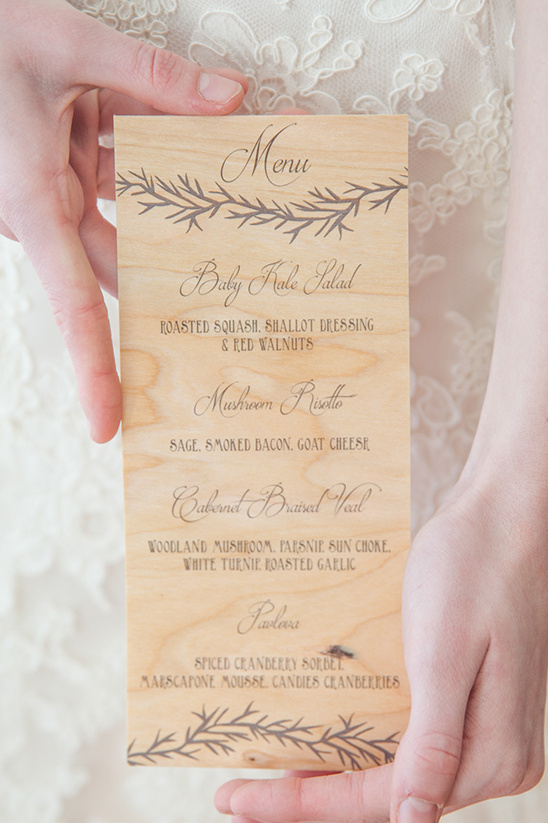 Wedding menu on wooden sign held by bride in elegant dress