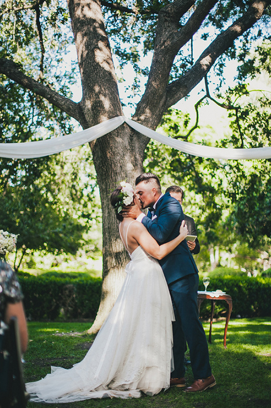Couple kissing at wedding ceremony under a large tree outdoors