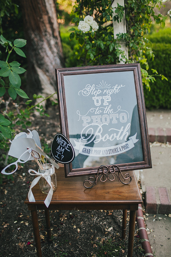 Wedding photo booth sign with props on a small wooden table