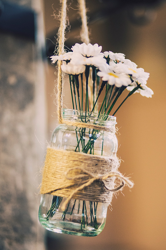 White daisies in a mason jar wrapped with twine, hanging