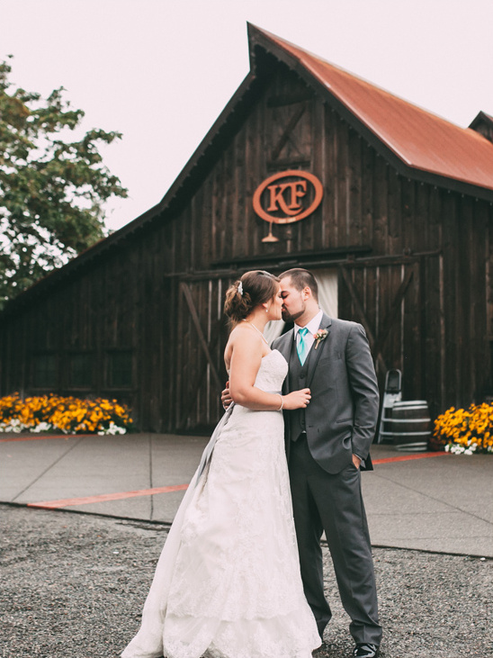 Bride and groom kissing in front of a rustic barn wedding
