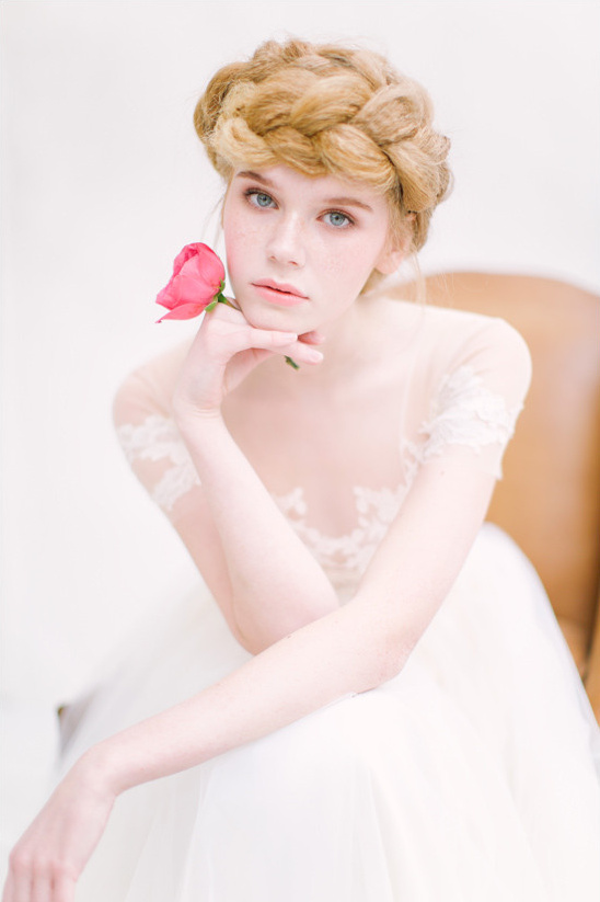 Elegant woman with braided hair holds a rose in her hand