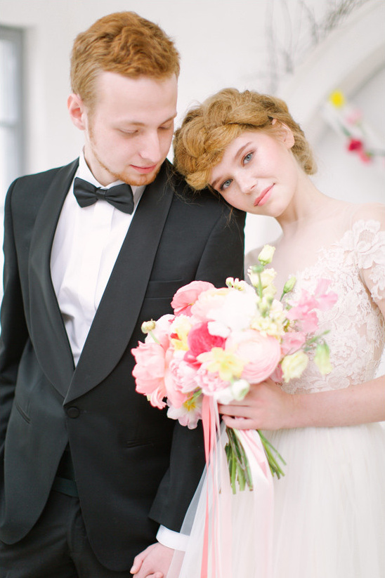 A newlywed couple posing tenderly, holding hands and a floral bouquet