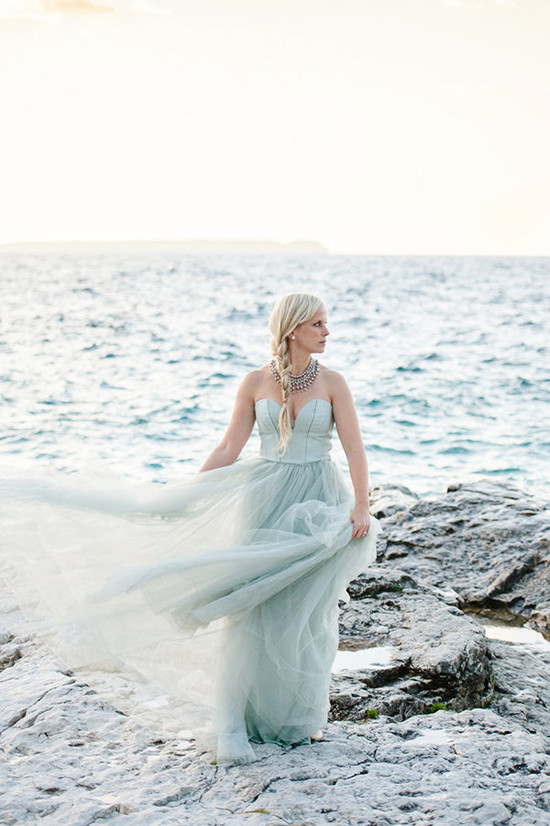 Woman in flowing seafoam dress on a rocky shoreline
