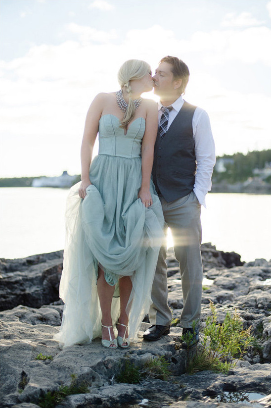 Bride and groom romantically kiss on a rocky shore