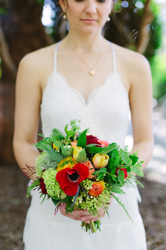 Bride holds vibrant wildflower bouquet in lace wedding dress