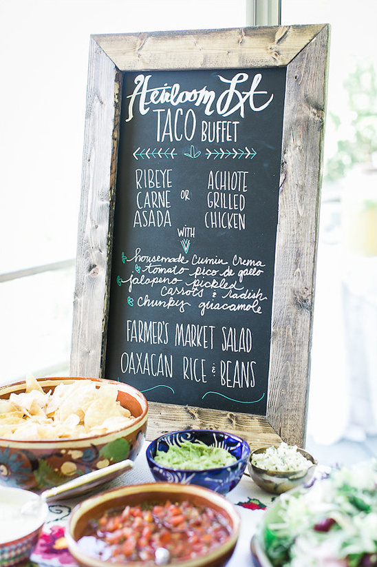 Taco buffet with menu on chalkboard and bowls of toppings