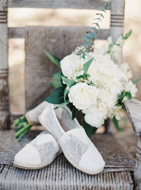 Lace bridal shoes and elegant white bouquet on a wooden chair