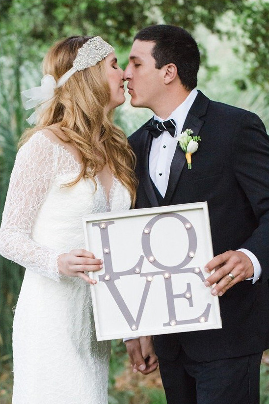 Newlyweds share a kiss holding a love sign at their wedding