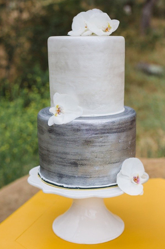 Two-tiered silver wedding cake decorated with white orchids on a stand