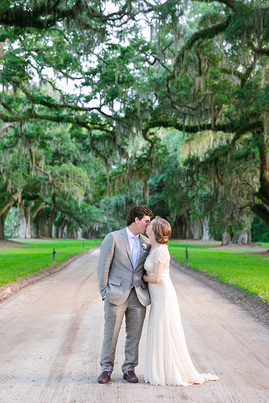 Bride and groom kissing under oak trees on wedding day