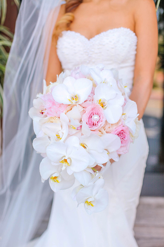 Bride holds a cascading bouquet of white orchids and roses
