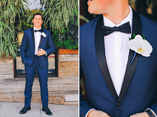 Groom in blue tuxedo with black bowtie and orchid boutonniere