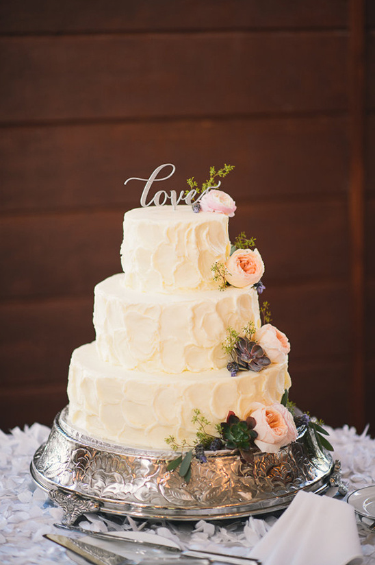 Three tier wedding cake with flowers and Love topper