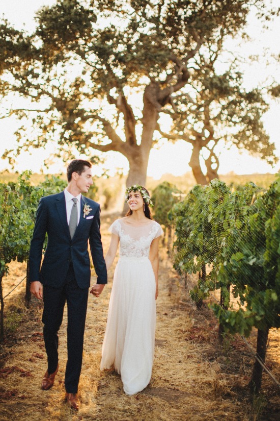 Bride and groom walk hand in hand in vineyard