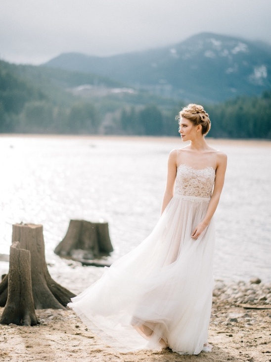 Bride in gown by lake with mountain backdrop