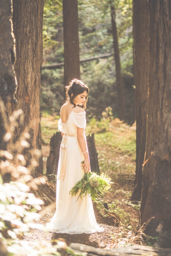 Bride in flowing gown holds bouquet in woodland setting