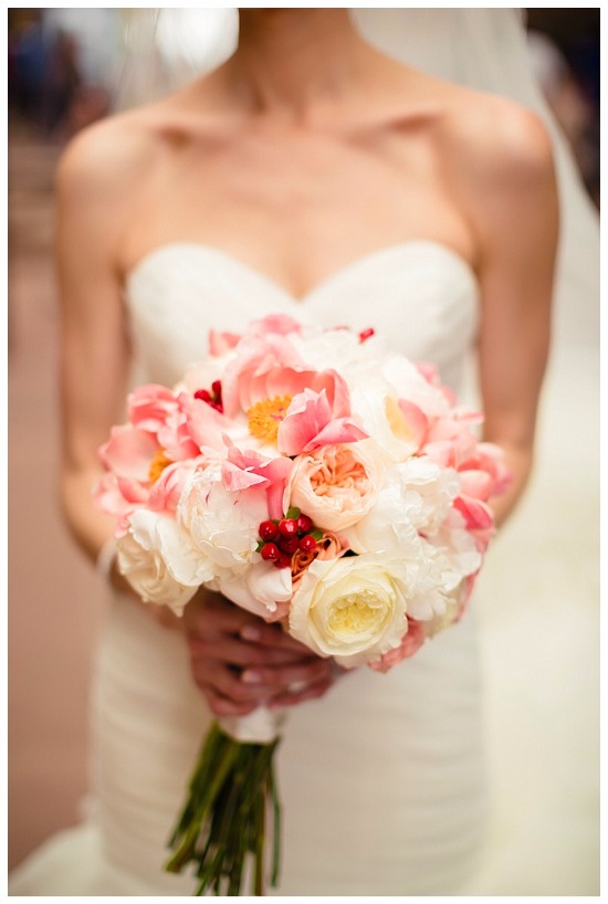 Bride in gown holds peony rose and berry bouquet