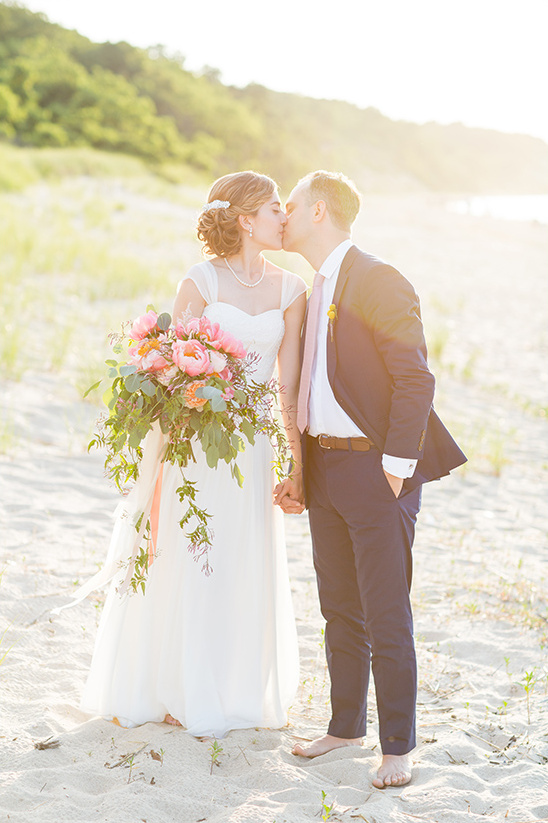 Bride and groom kissing on a sandy beach wedding day