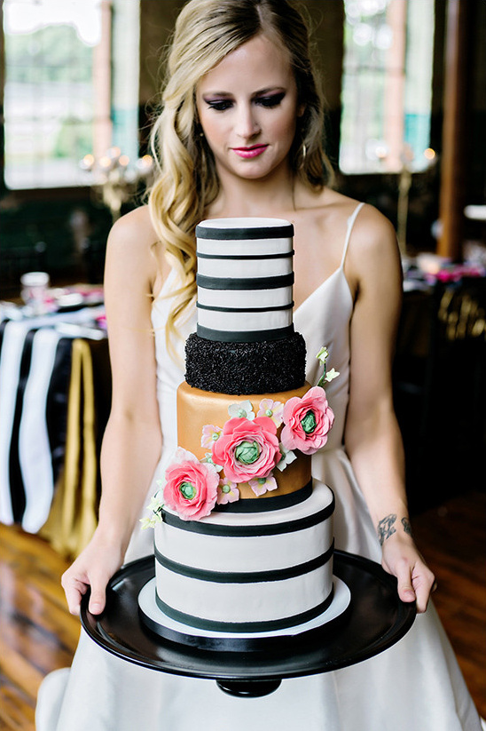 Bride holds striped tiered wedding cake with flowers