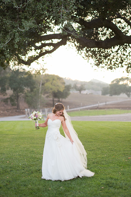 Bride in flowing gown on sunny grassy field at wedding
