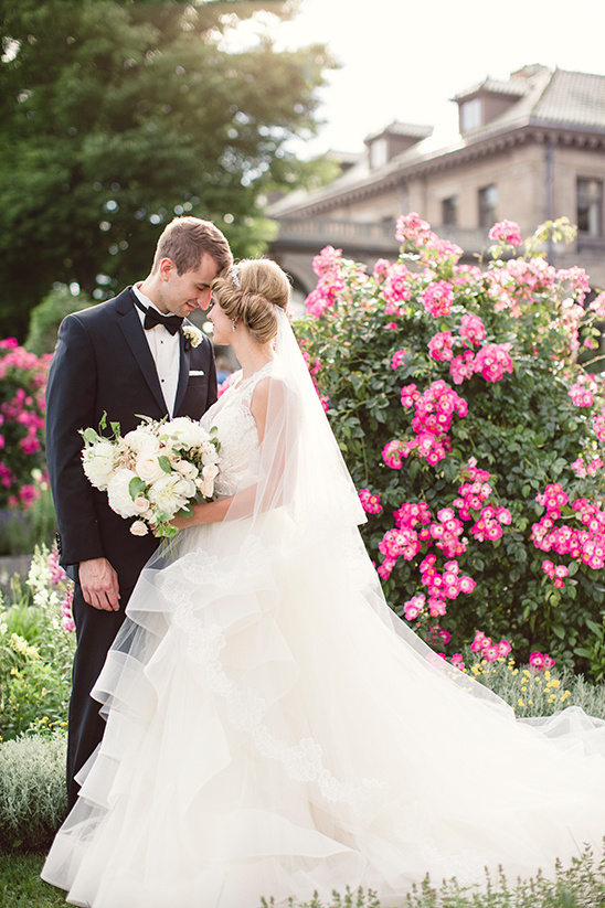 Bride and groom pose near pink roses on wedding day