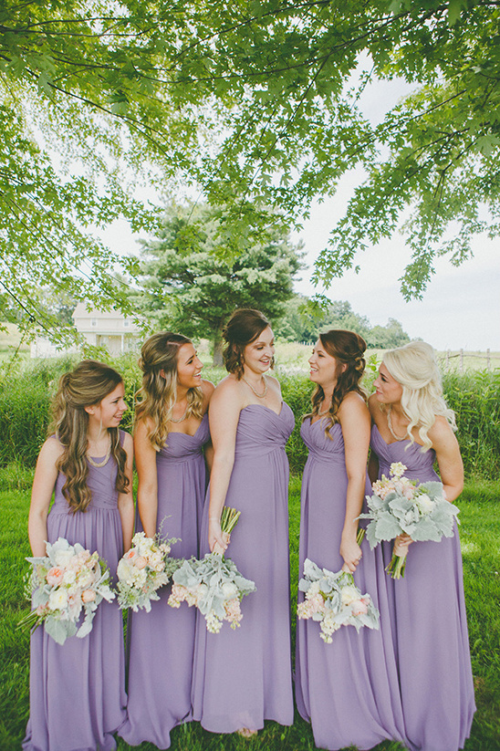 Bridesmaids in lavender dresses hold bouquets outdoors