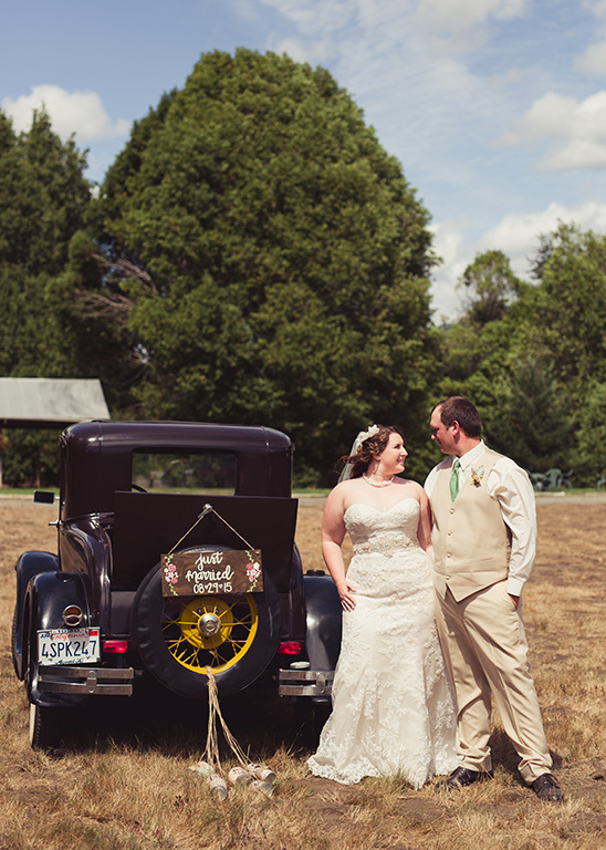 Happy couple posing beside a vintage car on their wedding day