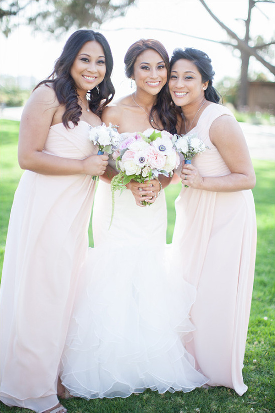 Bride and bridesmaids in blush gowns smile outdoors
