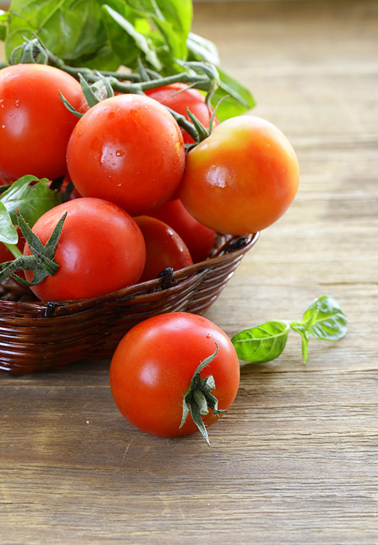Fresh cherry tomatoes and basil in a wicker basket