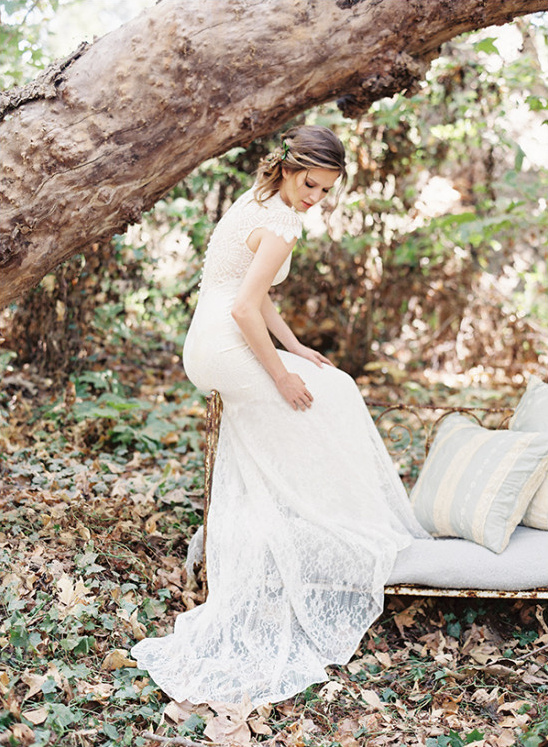 Bride in lace dress poses on a vintage bench in a forest