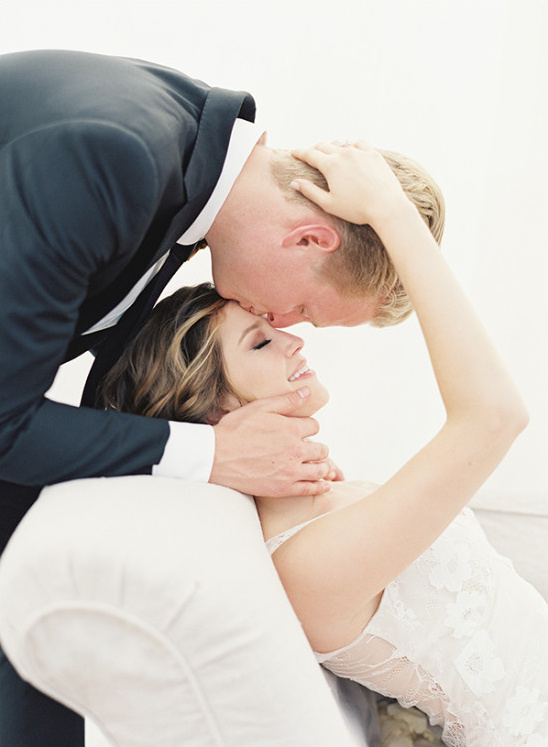 Groom kisses bride forehead in loving wedding moment
