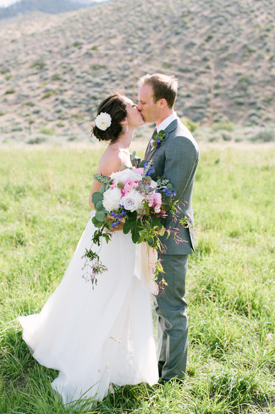 Bride and groom kissing, holding bouquet in field