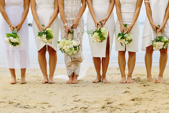Bridesmaids in white dresses holding bouquets on a beach