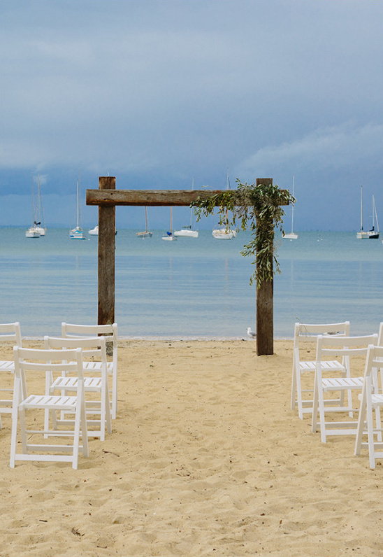 Beach wedding aisle with arbor and sailboats view