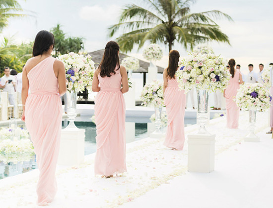 soft pink bridesmaids walking down a bright white aisle