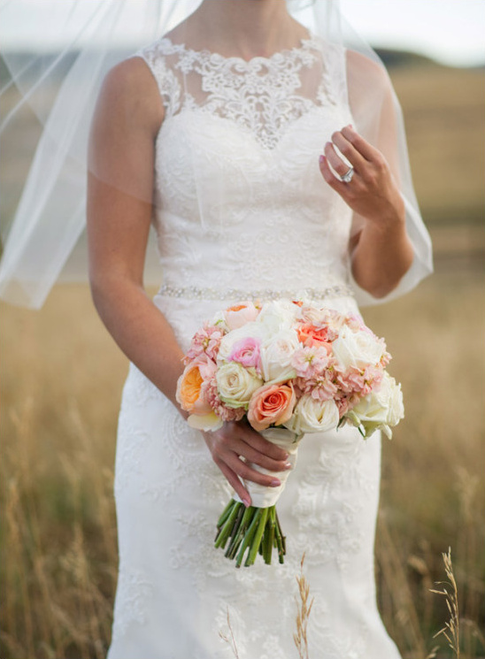 Bride in lace gown holding peach and white wedding bouquet