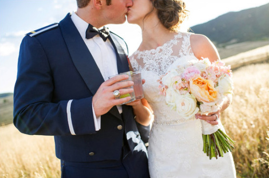 Bride and military groom kissing holding drinks bouquet