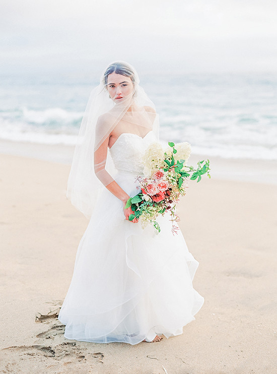 Bride in white gown holding flowers on beach wedding