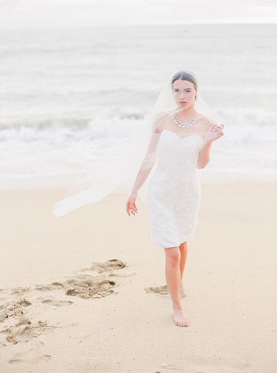 Beach bride in white dress walking barefoot on sand