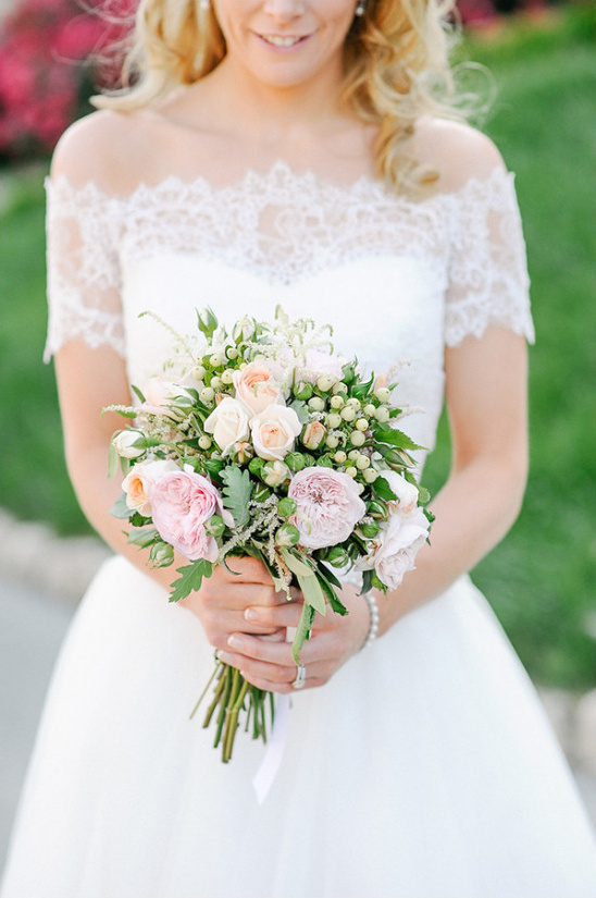 Bride holding a pastel rose bouquet in a lace wedding dress