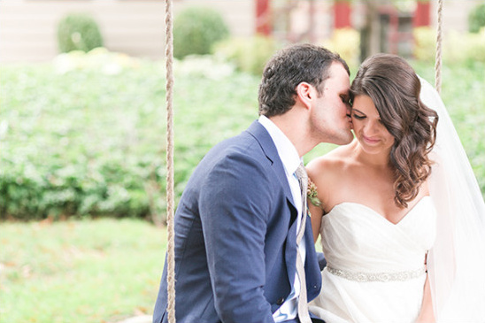 Groom kisses his bride on a swing at their wedding