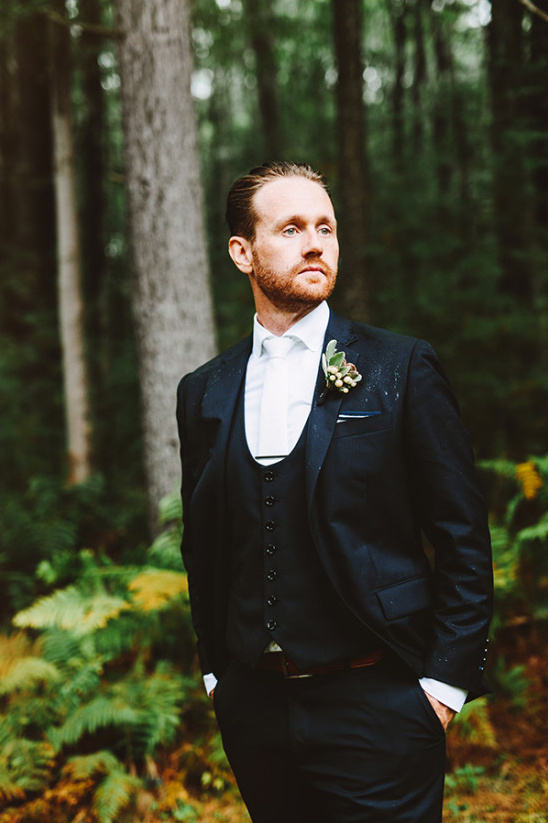 Groom in dark suit stands in a forest