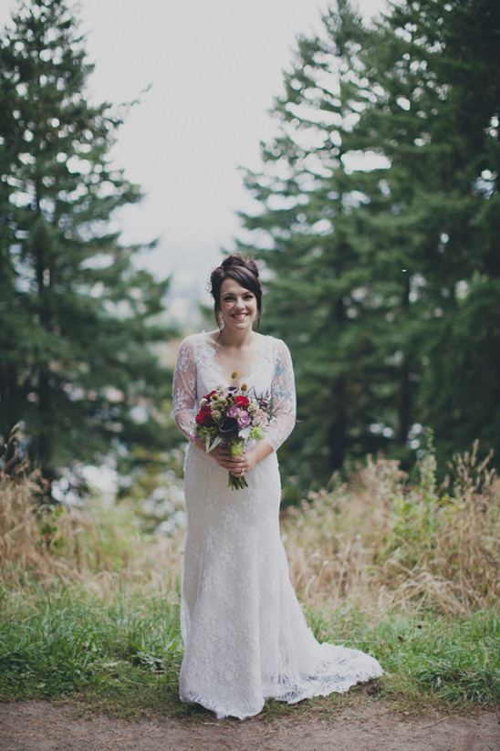 Bride in lace dress with bouquet at forest wedding