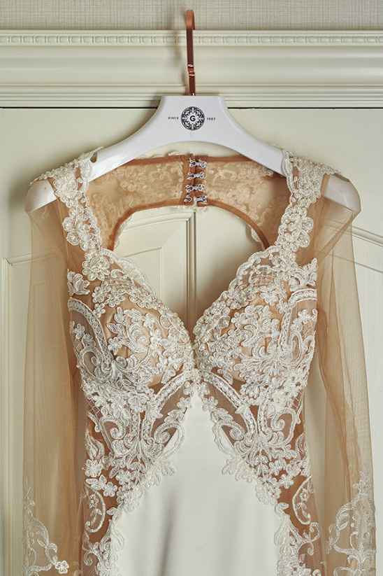 Lace detailed wedding dress hangs on a white door