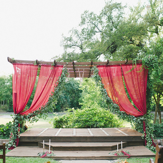 Outdoor wedding ceremony backdrop with red drapes and greenery