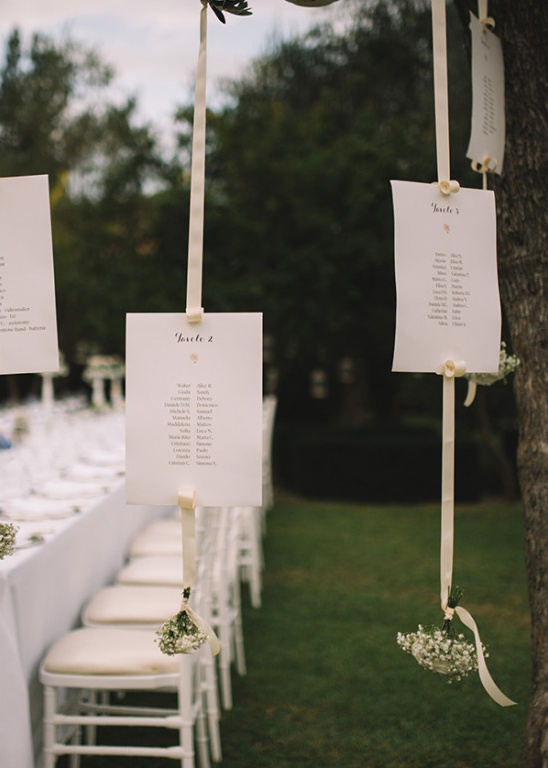 Elegant wedding seating chart hung with ribbons outdoors
