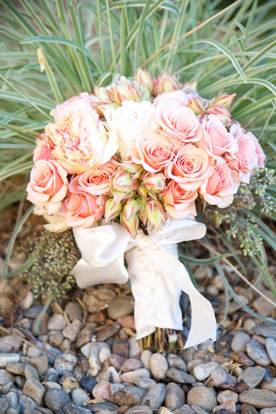 Peach rose wedding bouquet with white ribbon on rocks