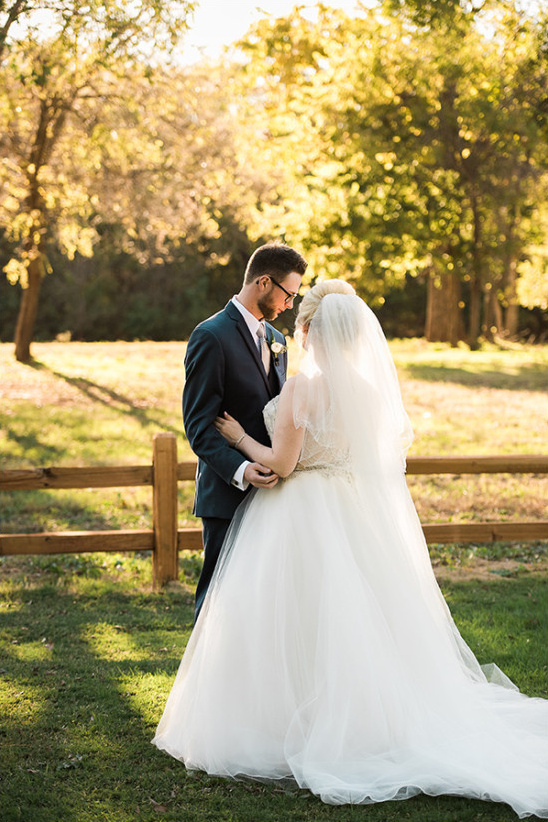 Bride and groom embrace in sunlit outdoor wedding scene